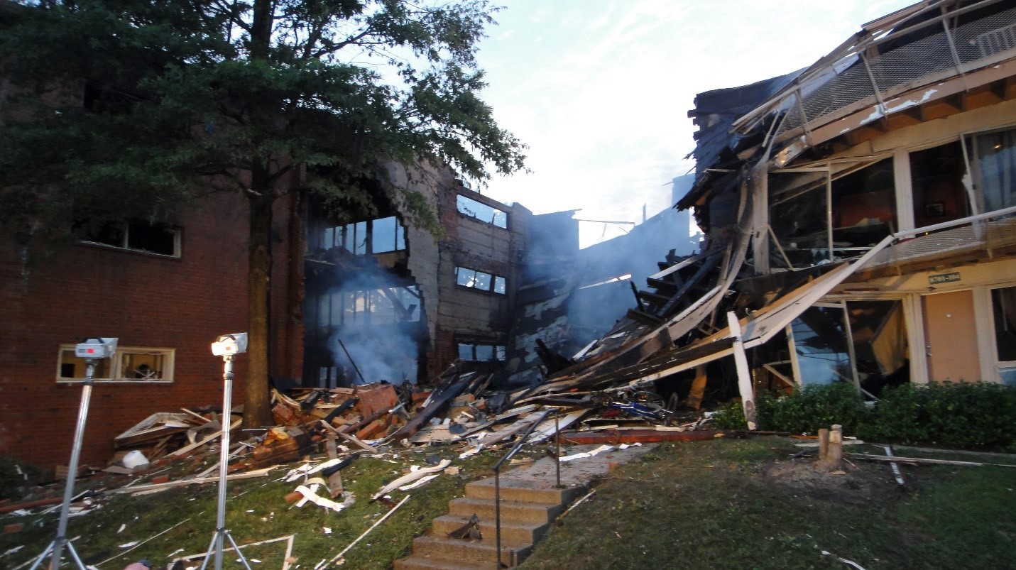 This front view of the accident scene shows two explosion-damaged buildings on Arliss Street, Silver Spring, Maryland. Building 8701 is located at the right center and building 8703 is located at the left of the photograph. Some smoke is seen at the accident scene. (Photo provided by Public Service Commission of Maryland)